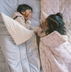 Two children cozy in Sleeping Bags Dusty Blue Gingham, ready for a fun sleepover or movie night.