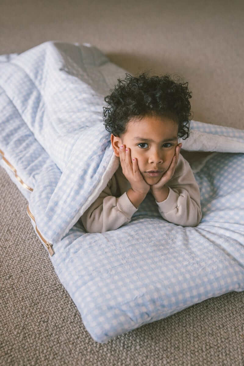 Sleeping Bag Dusty Blue Gingham with a child relaxing and cozy inside, perfect for comfort during slumber parties.