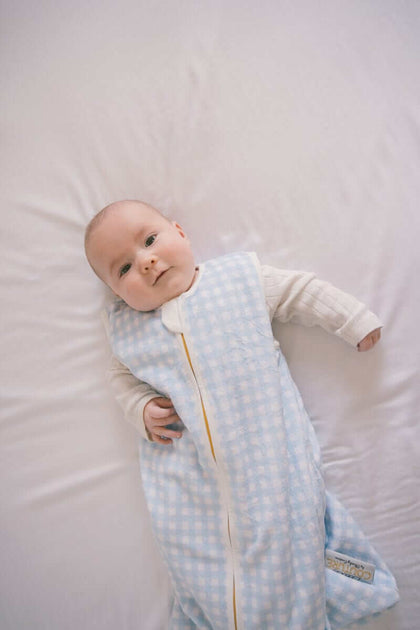 Baby wearing a Dusty Blue Gingham Wearable Minky Couture Blanket on a white bed.