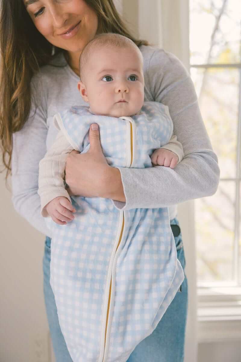 Mom holding a baby in a Dusty Blue Gingham Wearable Minky Blanket, showcasing its cozy and safe design.