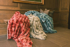 Three blankets, in red, light green, and blue, are draped over a wooden bench.
