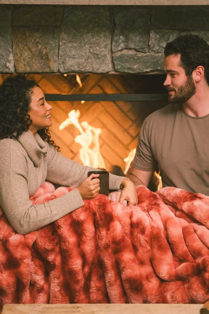 Couple sitting next to a fireplace while a Extreme Ultra Cloud Red Pear weighted blanket is draped over their laps.