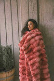 Young woman wrapped up in a two toned red weighted blanket standing against a wooden framed wall.