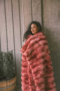 Young woman wrapped up in a two toned red weighted blanket standing against a wooden framed wall.