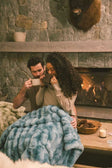 Couple sitting next to a fireplace with a cozy ocean blue Extreme Ultra Cloud Caribbean Holiday blanket.