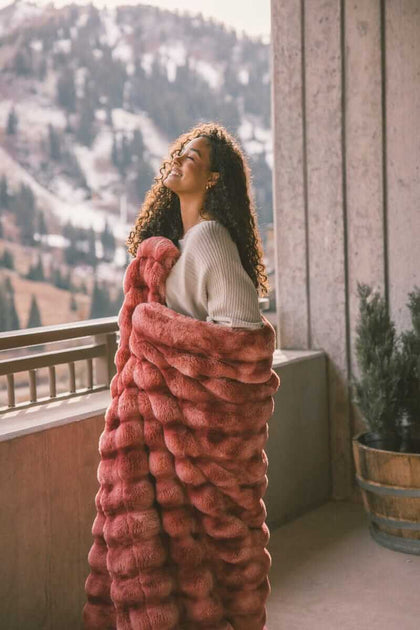 Woman wrapped up in Extreme Ultra Cloud Red Pear weighted blanket, standing on a balcony enjoying the view of the snowy mountains.