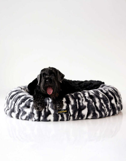 Black dog resting on a Minky Couture dog bed against a white background.