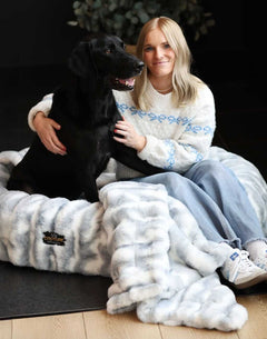 Woman sitting with a black dog on a Minky Couture weighted blanket in a cozy indoor setting.