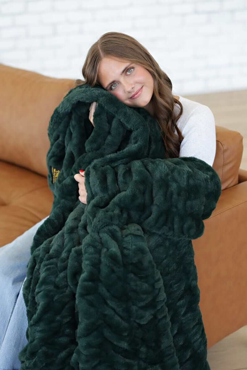 Cozy woman wrapped in a Hugs Pine Blanket, showcasing its rich dark green hue and plush texture.