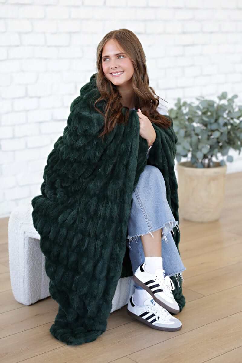 A woman wrapped in the Hugs Pine Blanket, featuring a rich dark green hue, styled for cozy warmth and comfort.