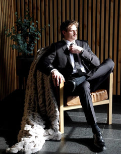 Man in suit sitting with Biggest Hugs Tranquil Dove Blanket draped over chair, showcasing luxury and comfort.