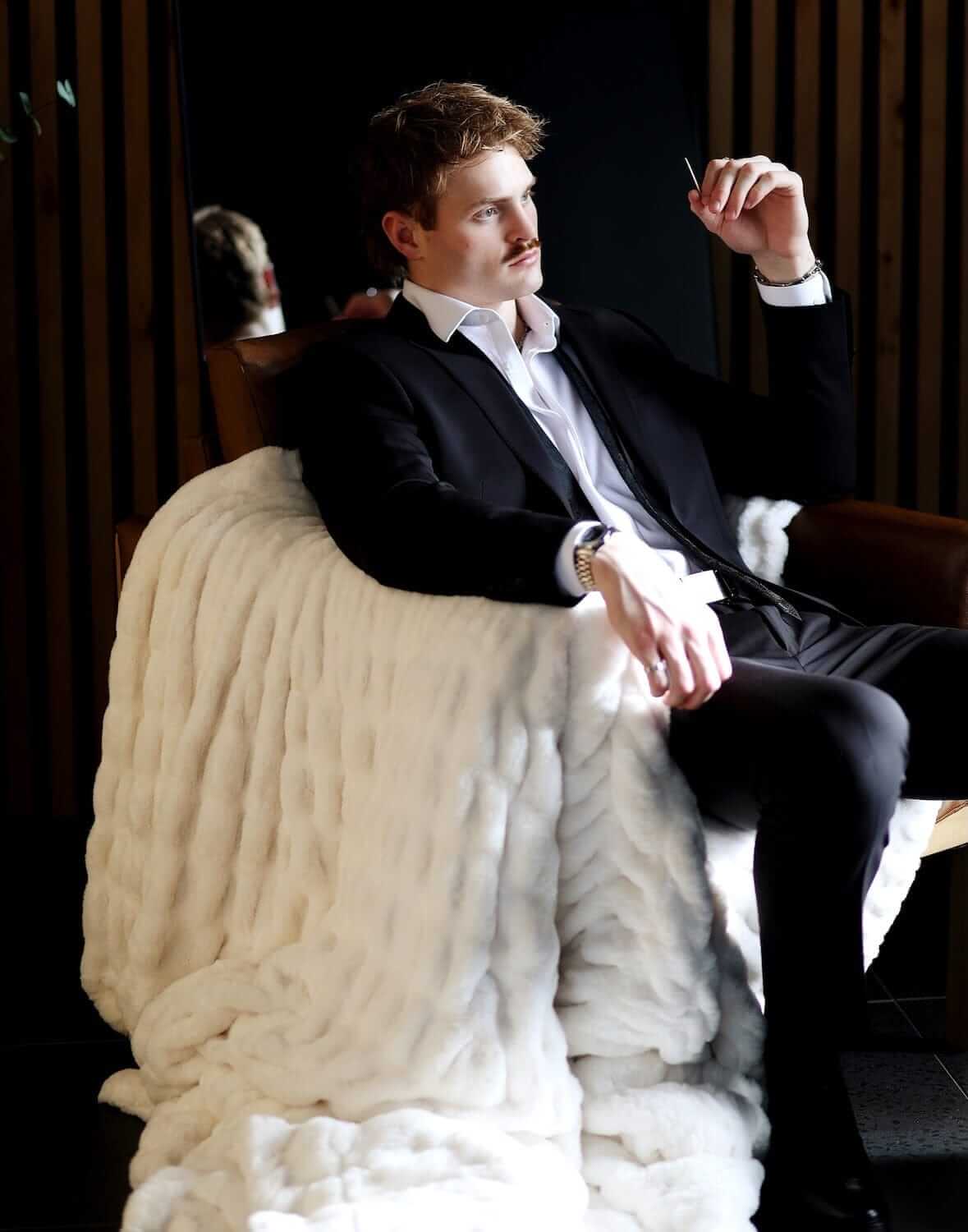 Man in a suit relaxing with the Biggest Hugs Cream weighted blanket draped over a chair, showcasing its comfort and elegance.