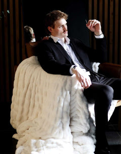 Man in a suit relaxing with the Biggest Hugs Cream weighted blanket draped over a chair, showcasing its comfort and elegance.