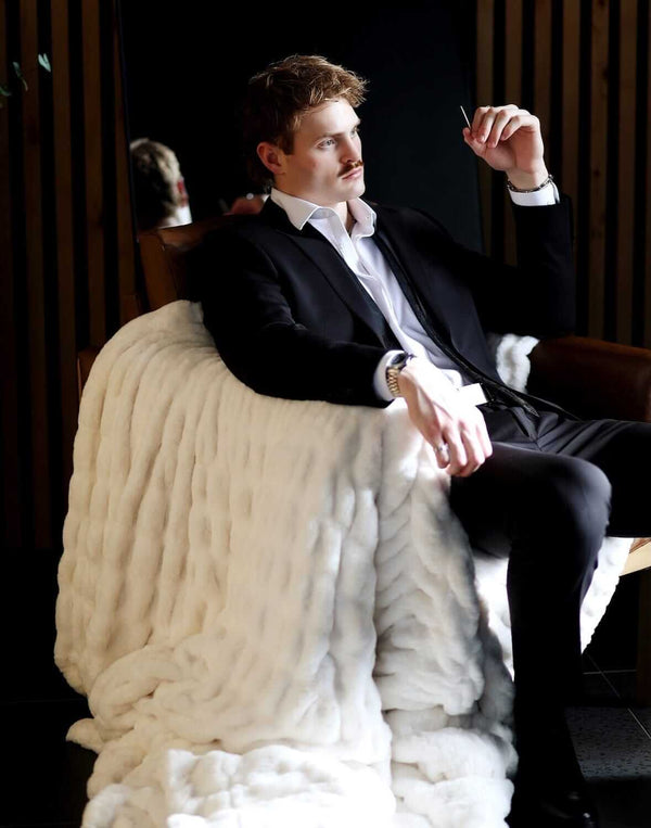Man in a suit relaxing with the Biggest Hugs Cream weighted blanket draped over a chair, showcasing its comfort and elegance.