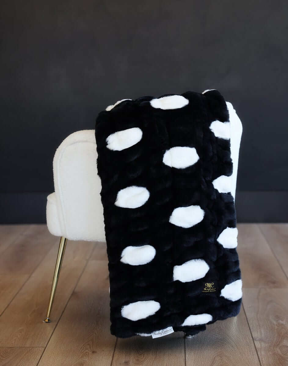 Hugs Polka Dot Black Minky Blanket with white spots draped over a cream chair.