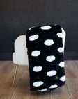 Hugs Polka Dot Black Minky Blanket with white spots draped over a cream chair.