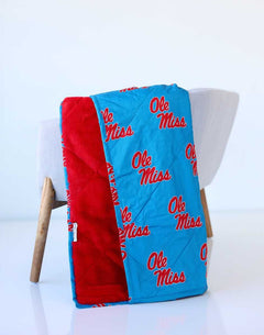 Ole Miss plush blanket draped over a chair, featuring blue fabric with red “Ole Miss” lettering and red backing.