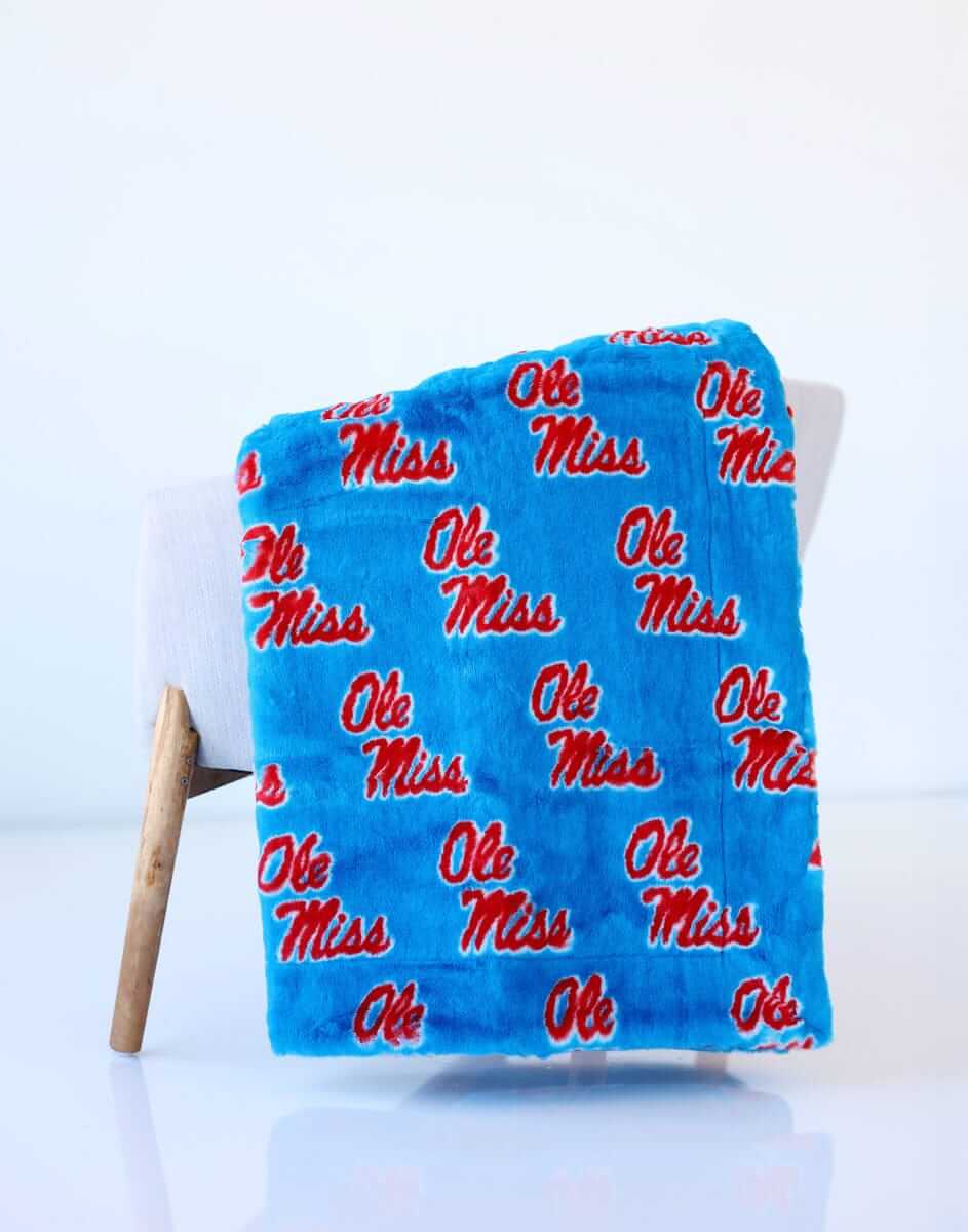 Ole Miss blue blanket draped over a chair, featuring repeating red “Ole Miss” lettering on soft fabric.