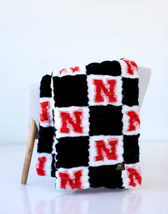 Nebraska Huskers checkerboard throw blanket in black, white, and red draped over a chair.