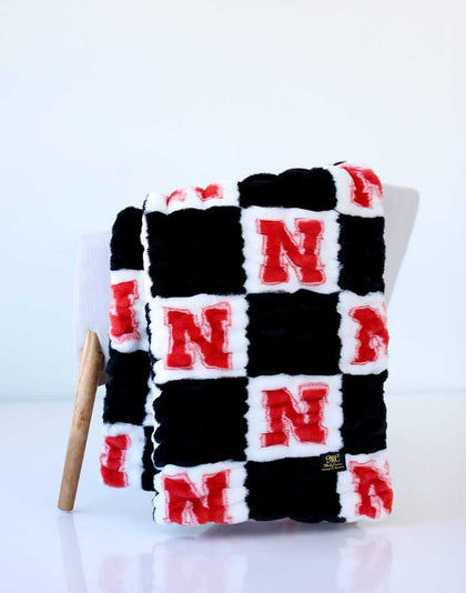 Nebraska Huskers checkerboard throw blanket in black, white, and red draped over a chair.