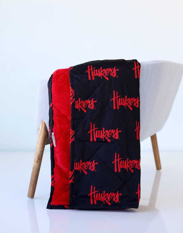 Nebraska Huskers throw blanket draped over chair, black exterior with red Huskers print and red lining.