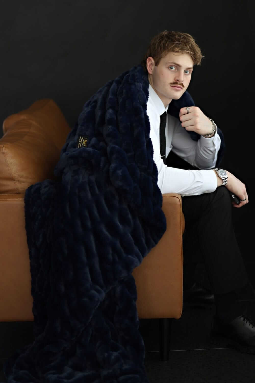 Man wrapped in the Biggest Hugs Navy weighted blanket sitting on a couch for ultimate comfort and style.