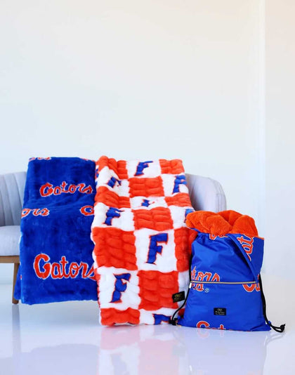 University of Florida Gators blankets in blue, orange, and white displayed on a chair with a matching drawstring bag.
