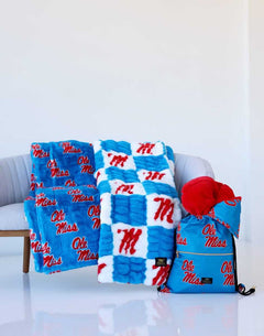 Ole Miss blanket set displayed on a chair, featuring blue and white throws with red logos and a matching drawstring bag.