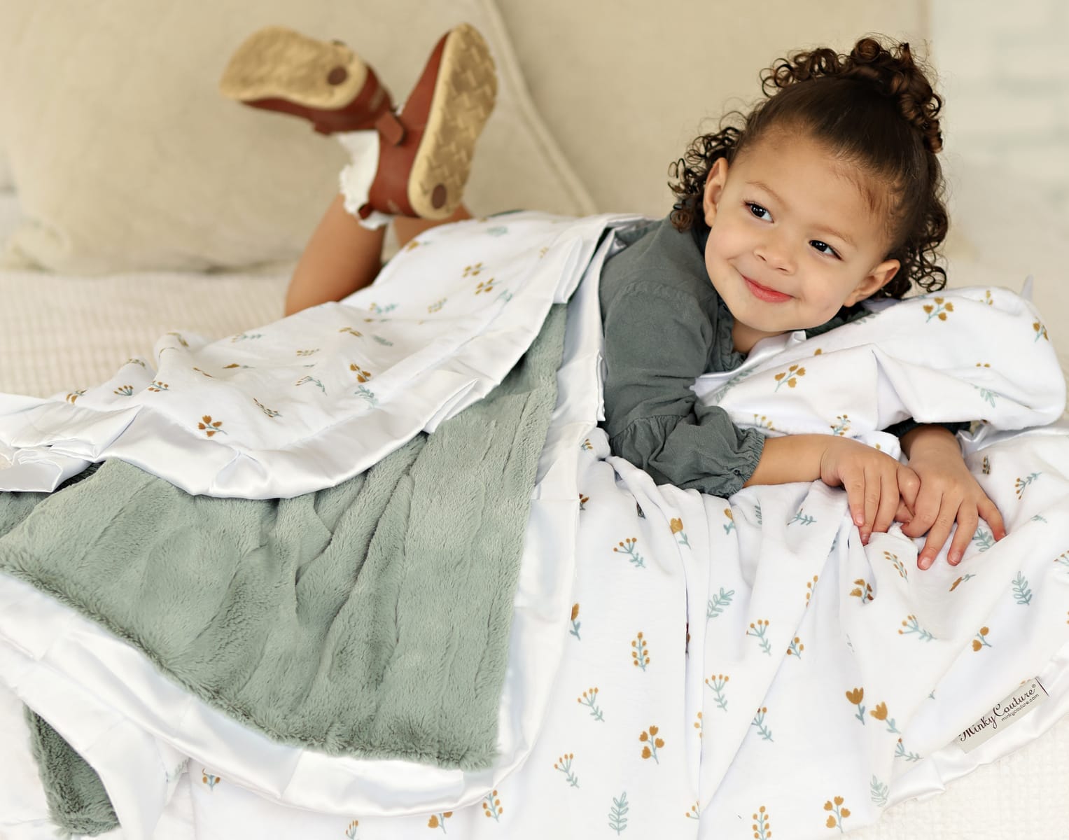 A child cozily wrapped in the Itsy Bitsy Flower Gold Blanket with a mist plush backing and white satin ruffle.