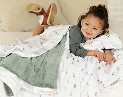 A child cozily wrapped in the Itsy Bitsy Flower Gold Blanket with a mist plush backing and white satin ruffle.