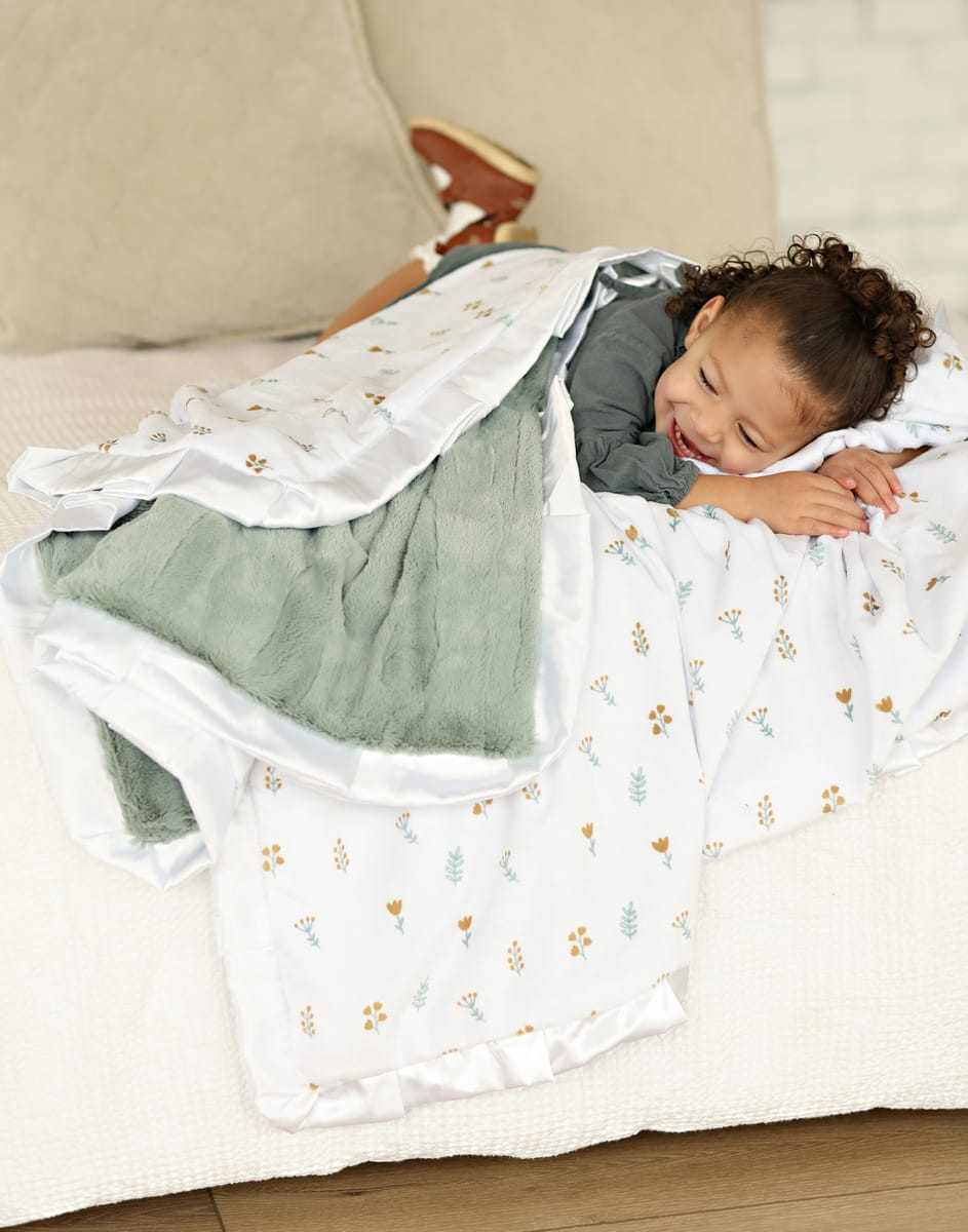 Child snuggled in Itsy Bitsy Flower Gold Blanket, featuring tiny flowers on a white background with a mist plush minky backing.
