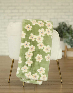 Lush Mist Floral Blanket draped over a white chair with golden legs, featuring a soft floral pattern on green fabric.