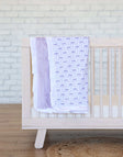 Minky Couture Lilac Ribbon Blanket draped over a crib, featuring purple bows on white with lavender plush backing.