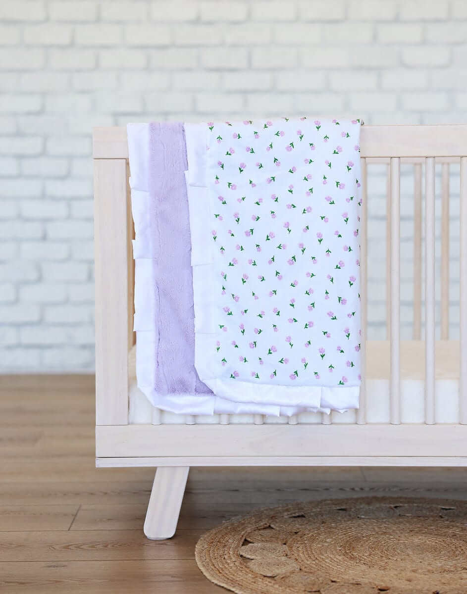 Minky Couture Itsy Bitsy Flower Lilac Blanket draped over a crib, featuring delicate purple flowers on a white background.