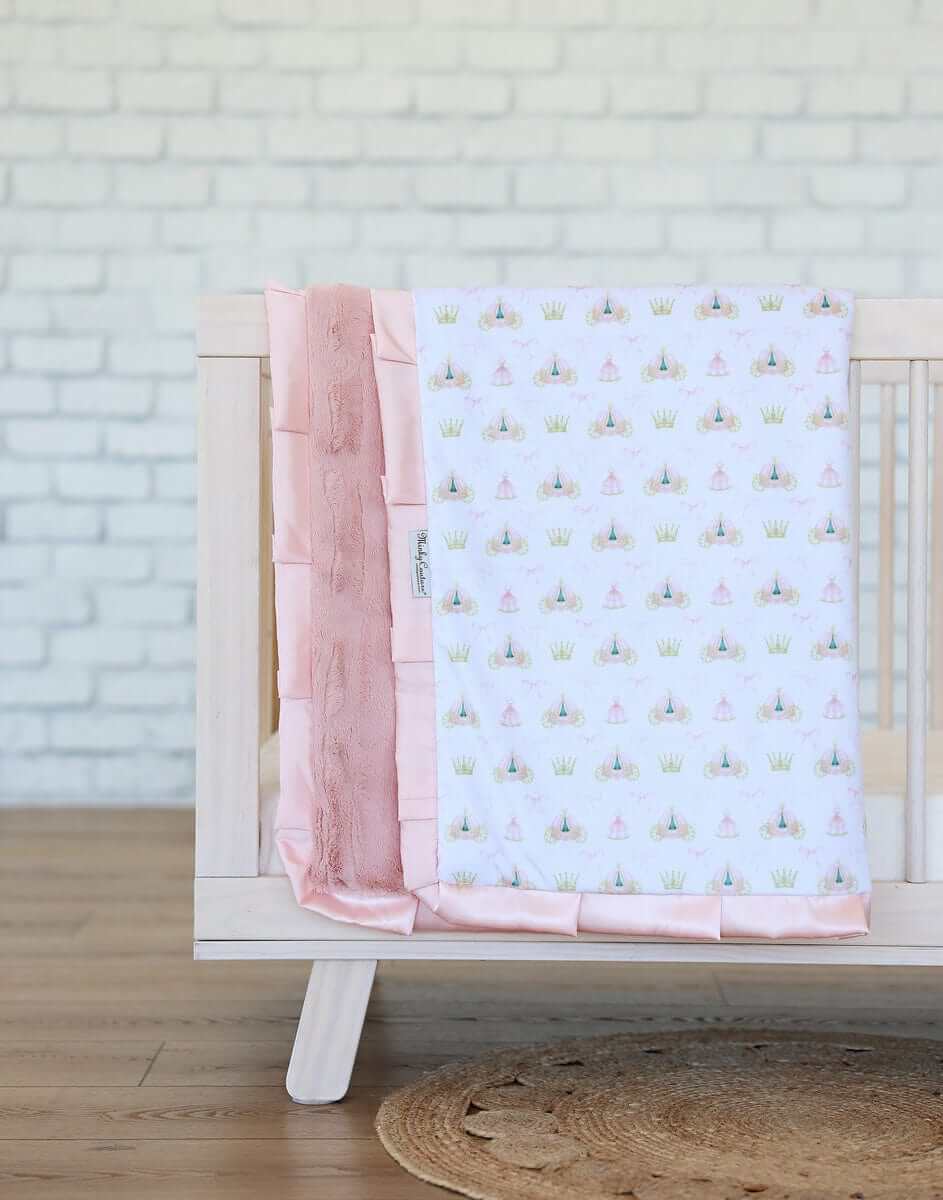 Princess Coach Blanket featuring crowns, bows, and carriages on a white background with apricot plush and satin ruffle.