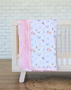 Minky Couture Princess Castle Blanket draped over a crib, featuring castles, unicorns, and a pink plush minky backing.