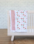 Minky Couture Cheery Cherry Blanket draped over a crib featuring cherry designs and a plush apricot backing.