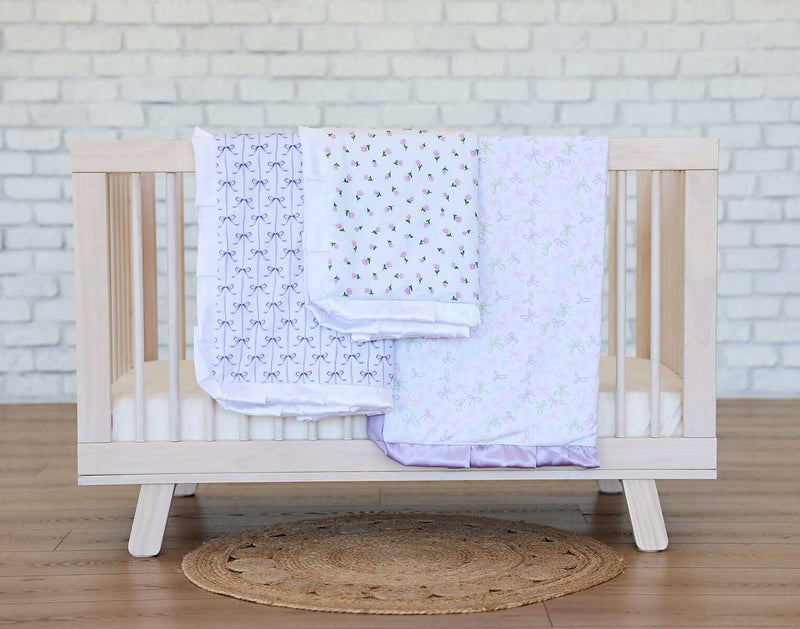 Lilac Ribbon Blanket displayed in a crib, showcasing its delicate purple bows and soft lavender minky backing.