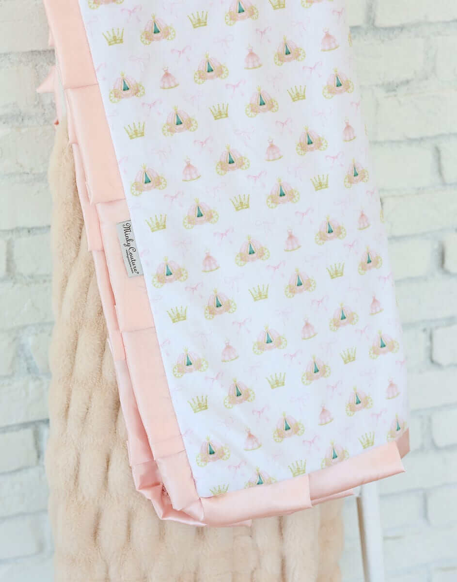 Minky Couture Princess Coach Blanket featuring crowns, bows, and royal carriages on a white background with apricot plush backing.