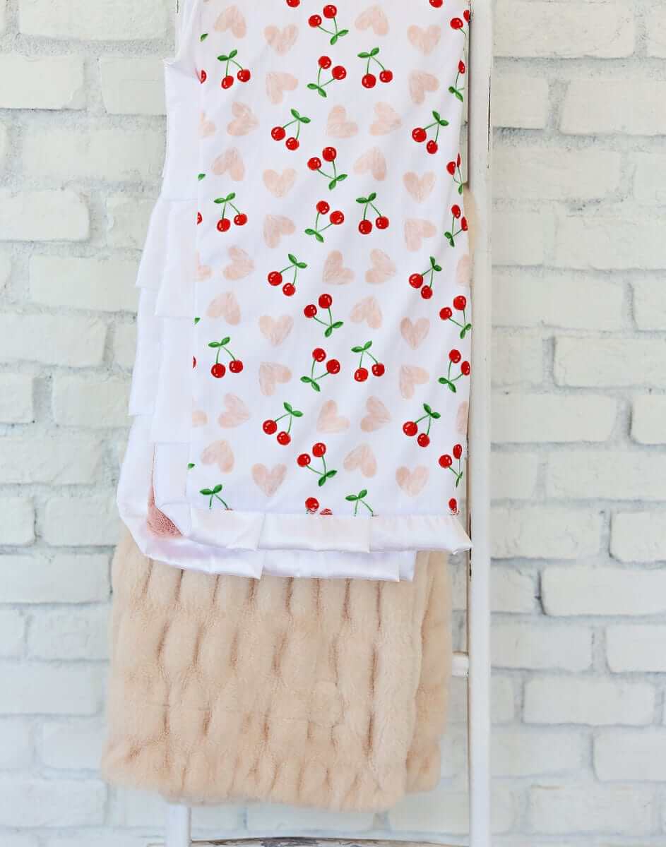 Cheery Cherry Blanket featuring bright red cherry pairs and pink hearts on a white background, with a plush apricot backing.