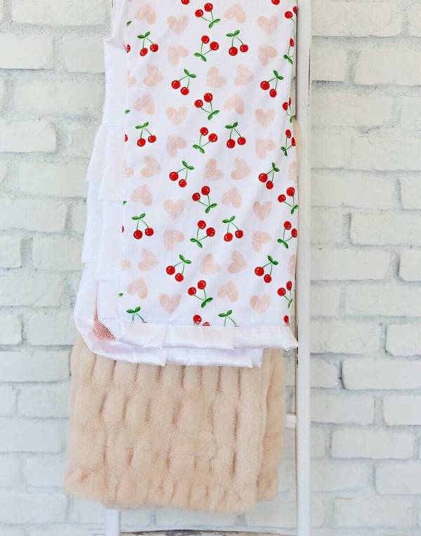 Cheery Cherry Blanket featuring bright red cherry pairs and pink hearts on a white background, with a plush apricot backing.