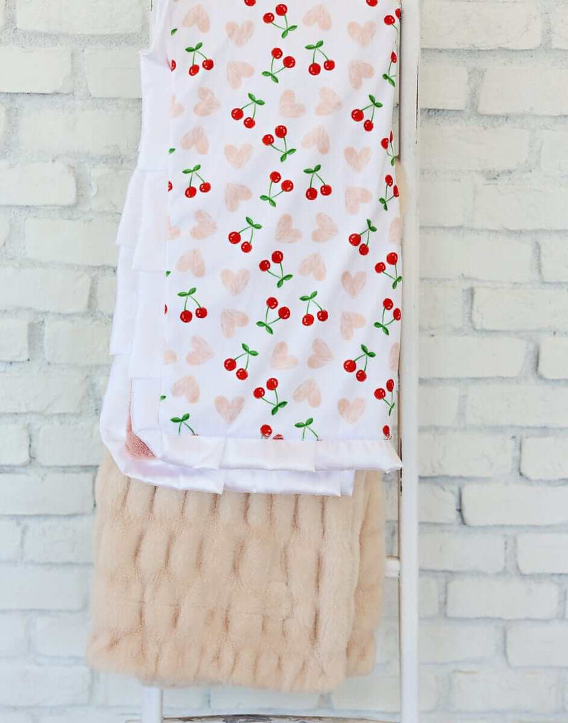 Cheery Cherry Blanket featuring bright red cherry pairs and pink hearts on a white background, with a plush apricot backing.
