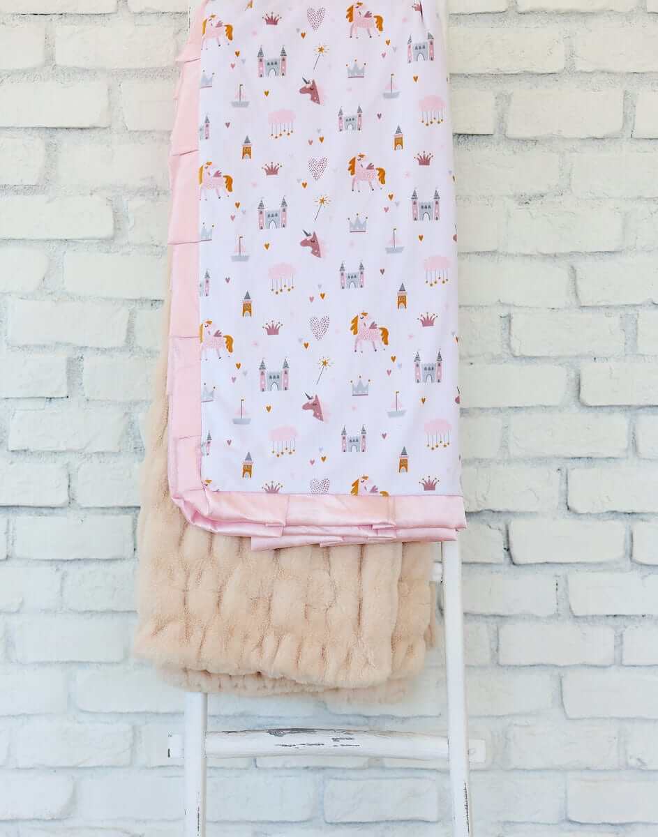 Princess Castle Blanket displayed on a chair, featuring whimsical designs of castles and unicorns with a pink satin ruffle.