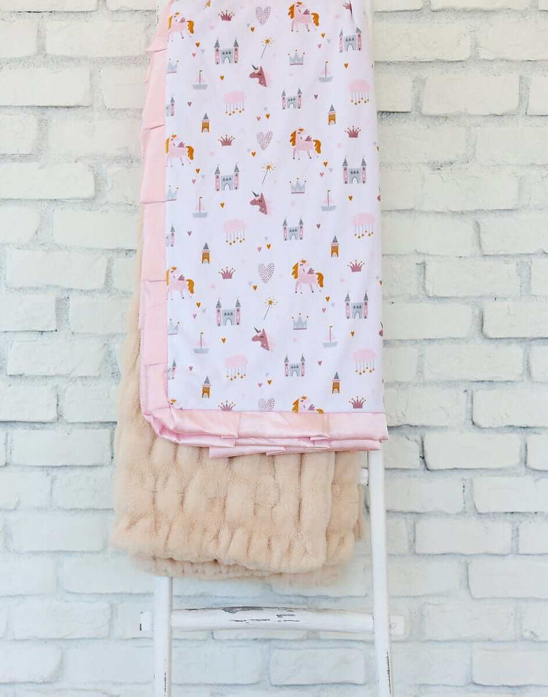 Princess Castle Blanket displayed on a chair, featuring whimsical designs of castles and unicorns with a pink satin ruffle.