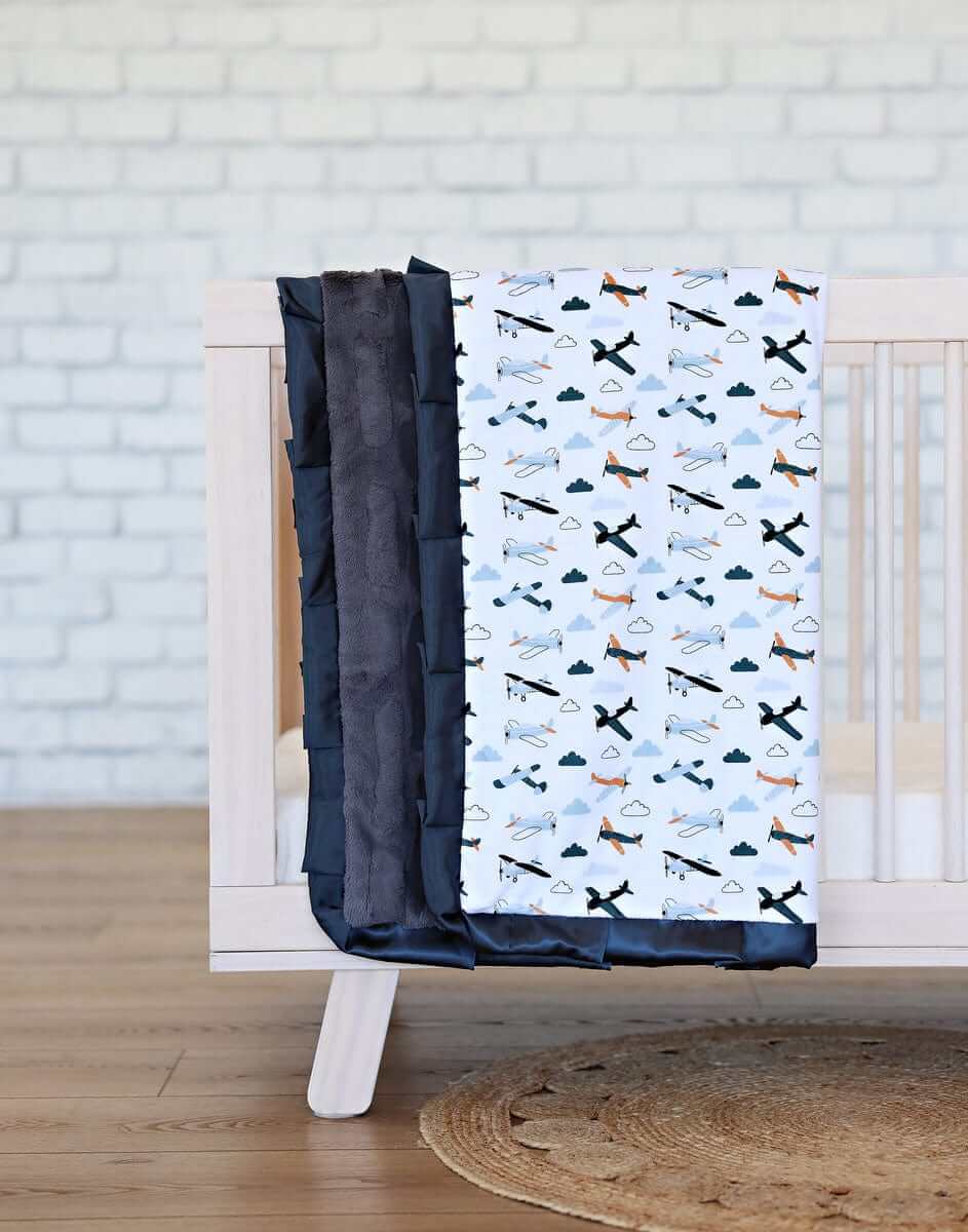 Airplane Blanket featuring small airplanes and clouds on a white background with a charcoal plush backing and satin ruffle.