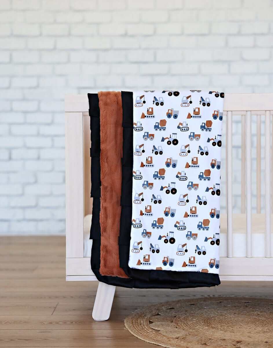 Bulldozer Blanket displayed on a crib, featuring excavators and mixers on a white background with a plush hazelnut backing.