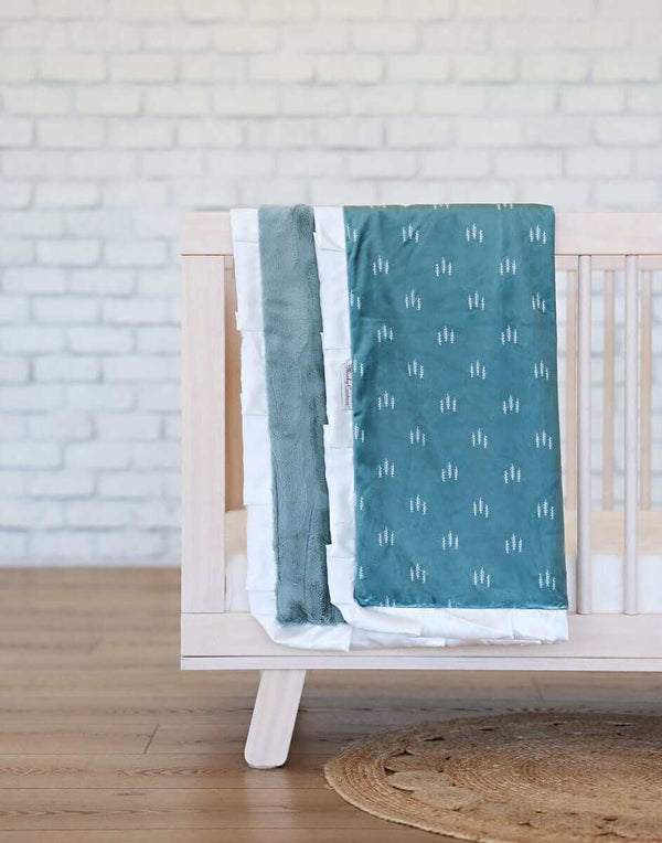 Itsy Bitsy Tree Blanket displayed on a crib, featuring a teal design, soft minky backing, and cream satin ruffle.