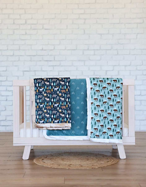 Wildlife Blanket displayed on a crib, featuring moose and cabin designs on a deep navy background.