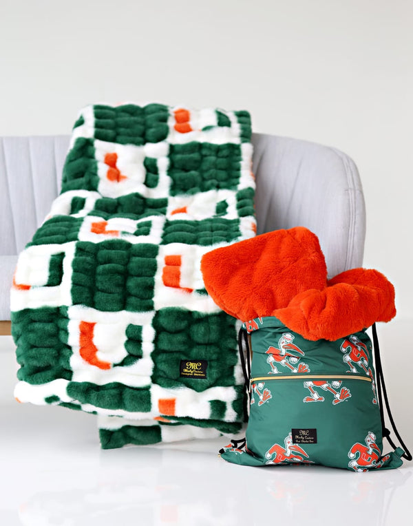Miami Hurricanes Hooded Stadium Everywhere Blanket displayed on a couch with vibrant orange and green design.