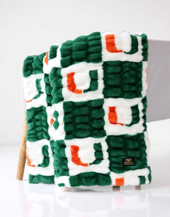 Green, white, and orange Miami Hurricanes Minky Couture blanket folded and draped over a chair, showing its textured pattern.